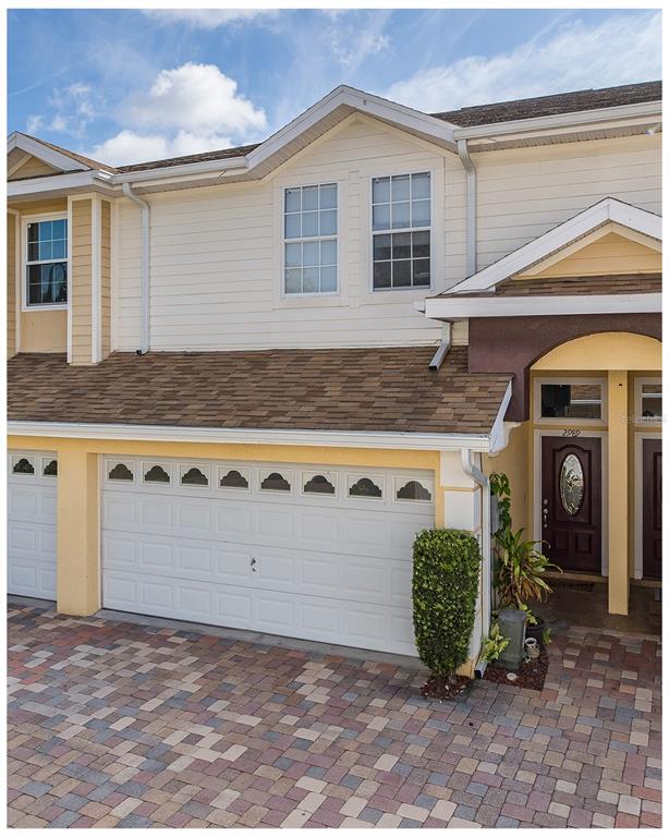 A two-story townhouse exterior features a white garage door, a brown front door, and pavers — 2989 ESTANCIA PLACE, CLEARWATER, FL