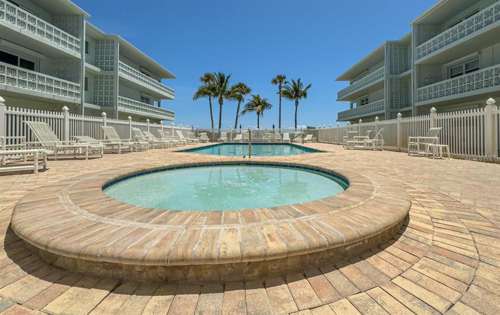 A circular hot tub sits in the foreground of a pool deck between two buildings — 4800 OCEAN BEACH BOULEVARD UNIT 226, COCOA BEACH, FL