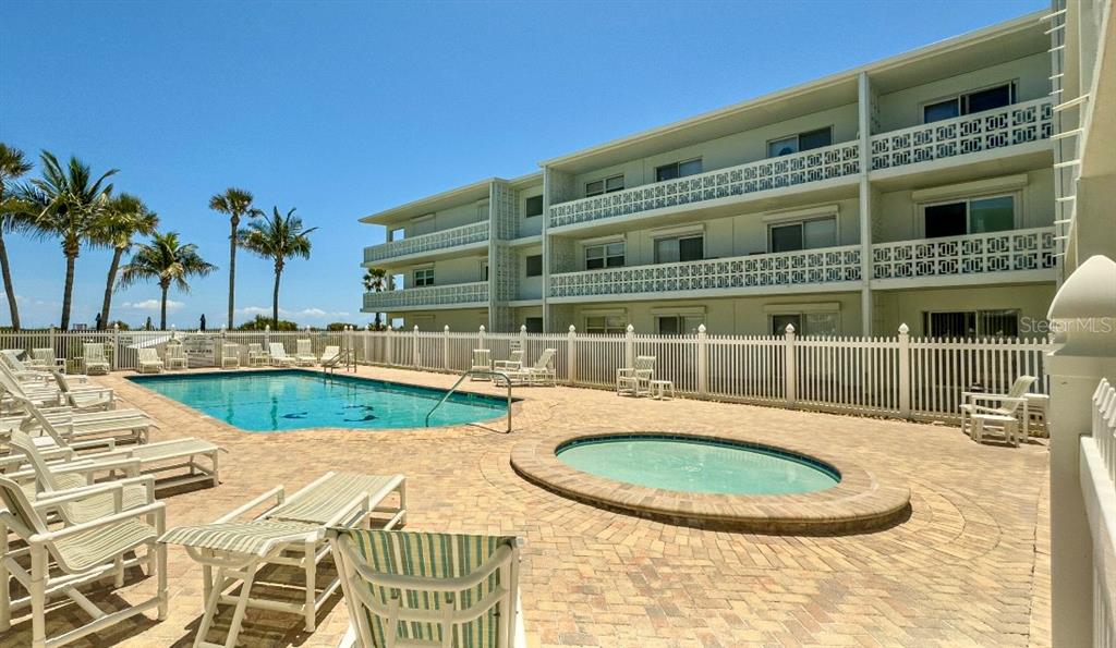 A multi-story building overlooks a swimming pool and a circular hot tub on a patio — 4800 OCEAN BEACH BOULEVARD UNIT 226, COCOA BEACH, FL