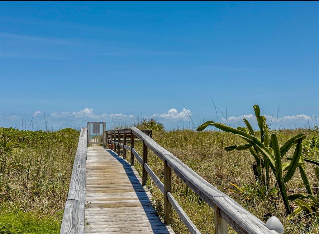 A wooden boardwalk with railings leads toward a gate surrounded by coastal vegetation — 4800 OCEAN BEACH BOULEVARD UNIT 226, COCOA BEACH, FL
