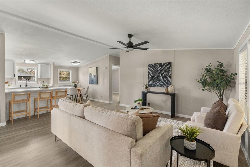 An open-concept living room and kitchen featuring light wood flooring, neutral walls, and modern furniture — 8110 TOM COSTINE ROAD, LAKELAND, FL