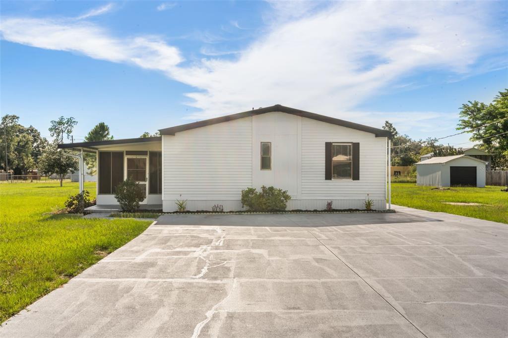 A white manufactured home features a screened-in porch and a large concrete driveway — 8110 TOM COSTINE ROAD, LAKELAND, FL