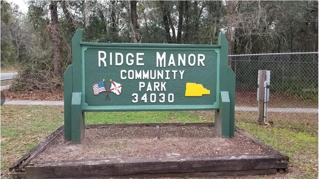 A green wooden sign for Ridge Manor Community Park stands on a mulched base — RIDGE MANOR BOULEVARD, DADE CITY, FL
