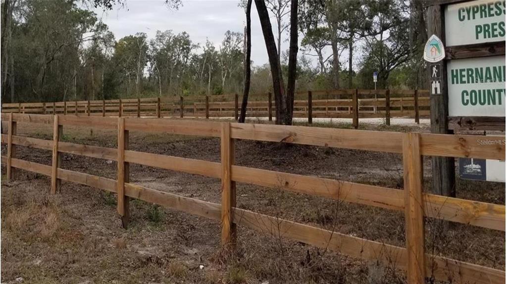 A wooden split-rail fence borders a wooded area with a Hernando County park sign — RIDGE MANOR BOULEVARD, DADE CITY, FL