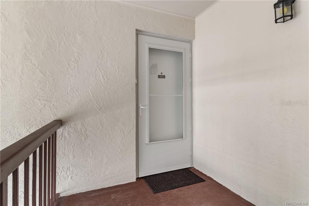 A white front door with a glass insert is set into a textured stucco wall — 2400 FOREST DRIVE UNIT 221, INVERNESS, FL