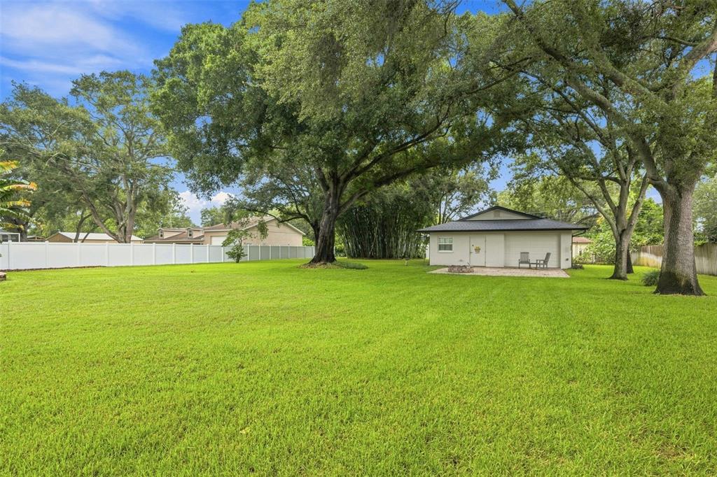 A large grassy backyard features mature oak trees, a white fence, and a detached garage — 13123 108TH AVENUE, LARGO, FL