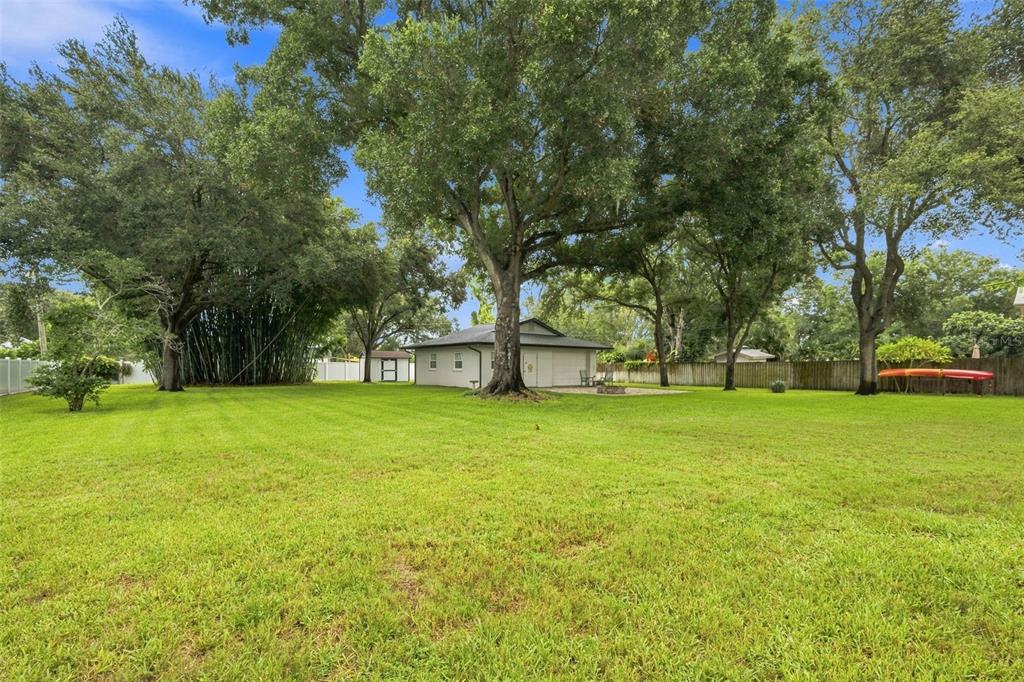 A large grassy backyard features mature trees, a detached garage, and a wooden fence — 13123 108TH AVENUE, LARGO, FL