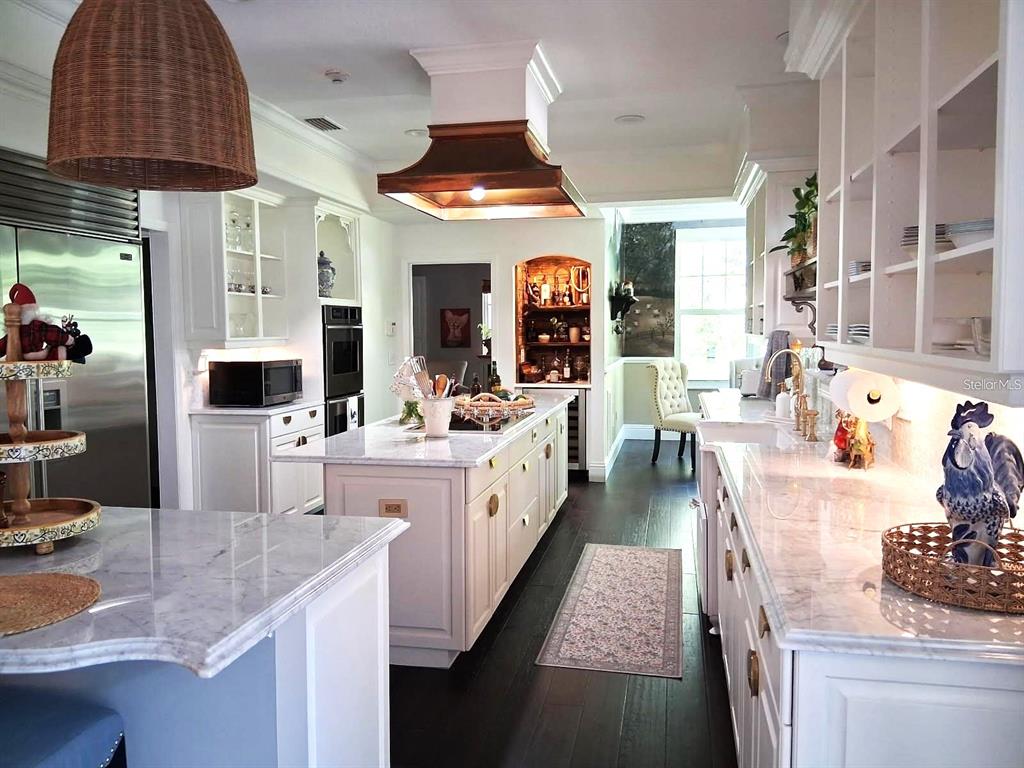 A bright kitchen features white cabinetry, marble countertops, a copper range hood, and dark flooring — 3171 DICK WILSON DRIVE, SARASOTA, FL