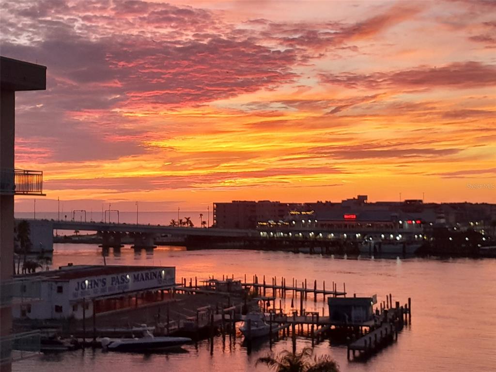 An elevated view of a marina and bridge at sunset with a vibrant orange sky — 1 KEY CAPRI UNIT 502E, TREASURE ISLAND, FL