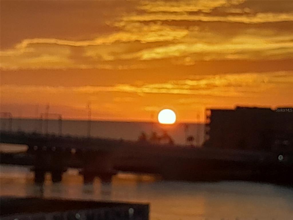 A sunset view over a body of water with a bridge and building silhouettes — 1 KEY CAPRI UNIT 502E, TREASURE ISLAND, FL
