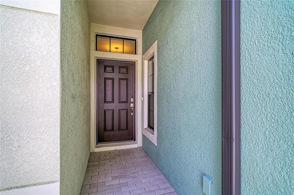 A covered entryway features a dark brown front door, a transom window, and teal stucco walls — 4991 OARSMAN COURT, SARASOTA, FL