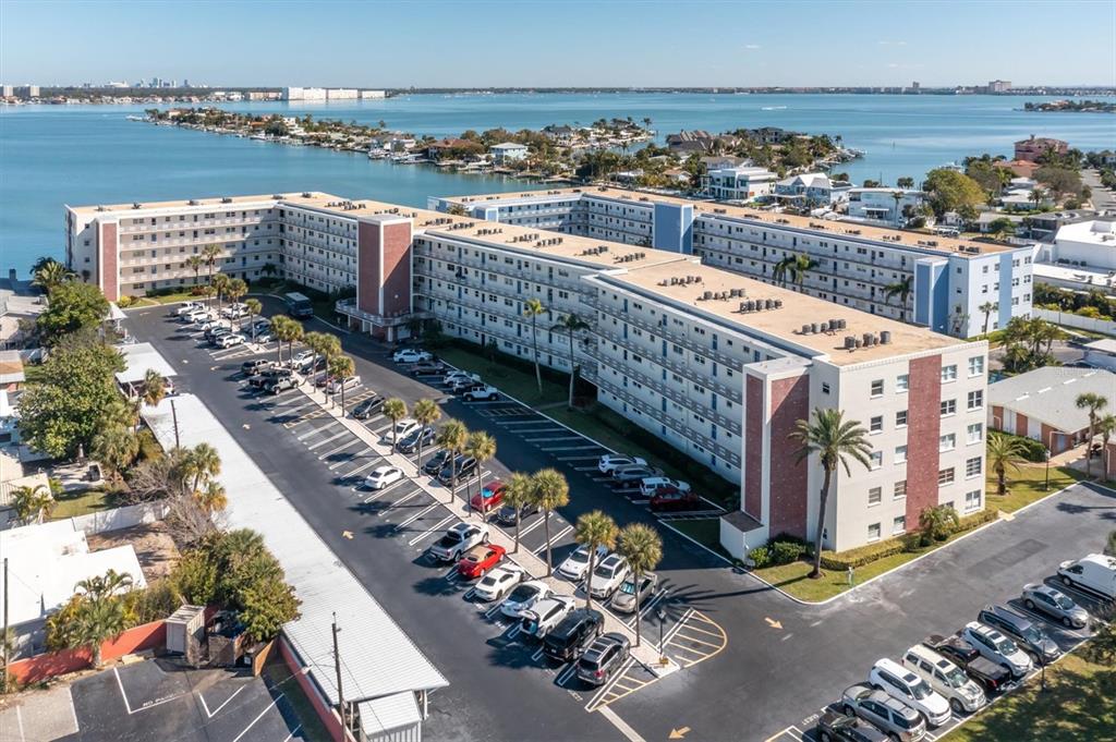 An aerial view shows a large apartment complex with a parking lot and waterfront — 5575 GULF BOULEVARD UNIT 337, ST PETE BEACH, FL