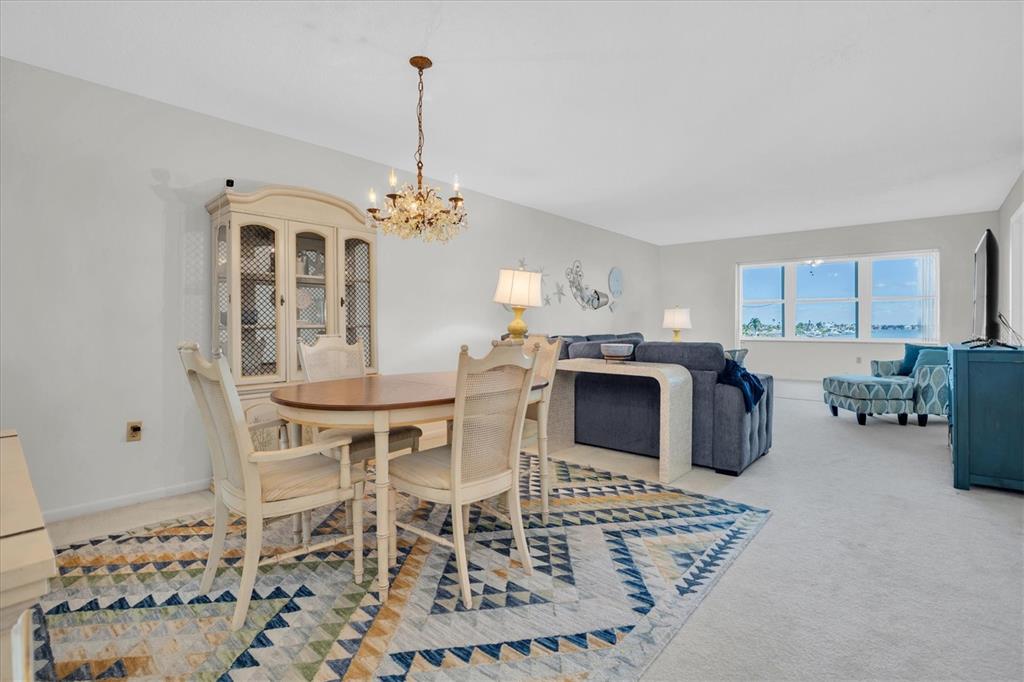 A dining area and living room with a blue sofa, patterned rug, and water view — 5575 GULF BOULEVARD UNIT 337, ST PETE BEACH, FL