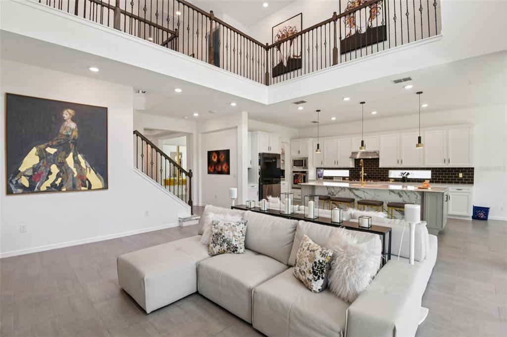 A spacious open-concept living room and kitchen featuring a large sectional sofa and lofted balcony — 11473 OWASEE TRAILS PLACE, RIVERVIEW, FL
