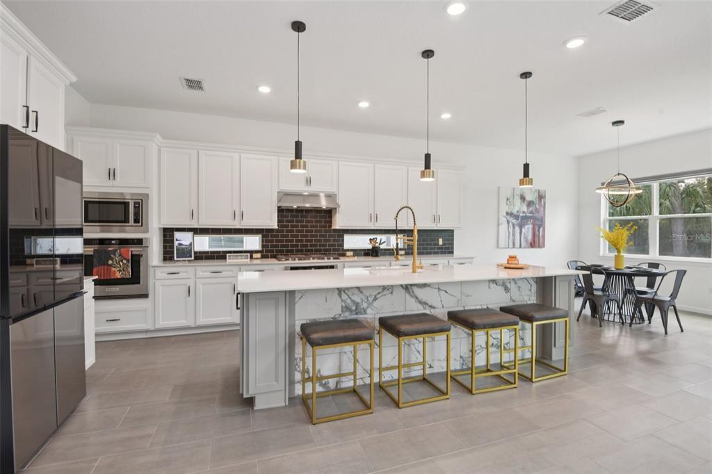 A modern kitchen features white cabinetry, a marble-topped island with bar stools, and dark tile — 11473 OWASEE TRAILS PLACE, RIVERVIEW, FL