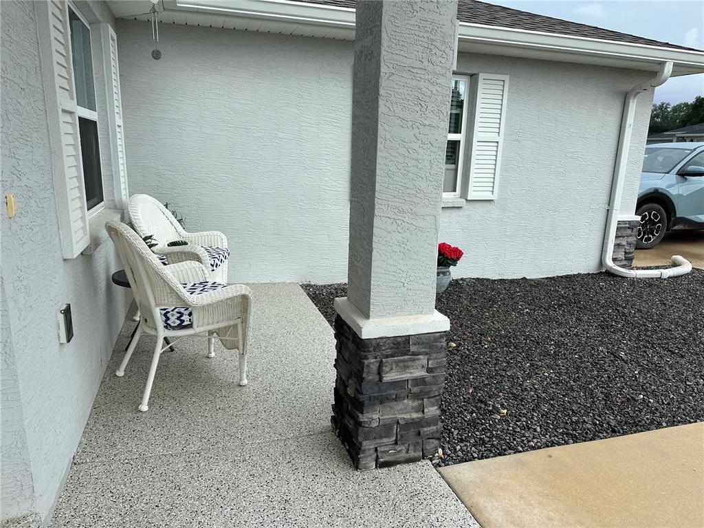 A covered front porch features a concrete floor, two white wicker chairs, and a stone pillar — 4322 E MARYLAND STREET, INVERNESS, FL
