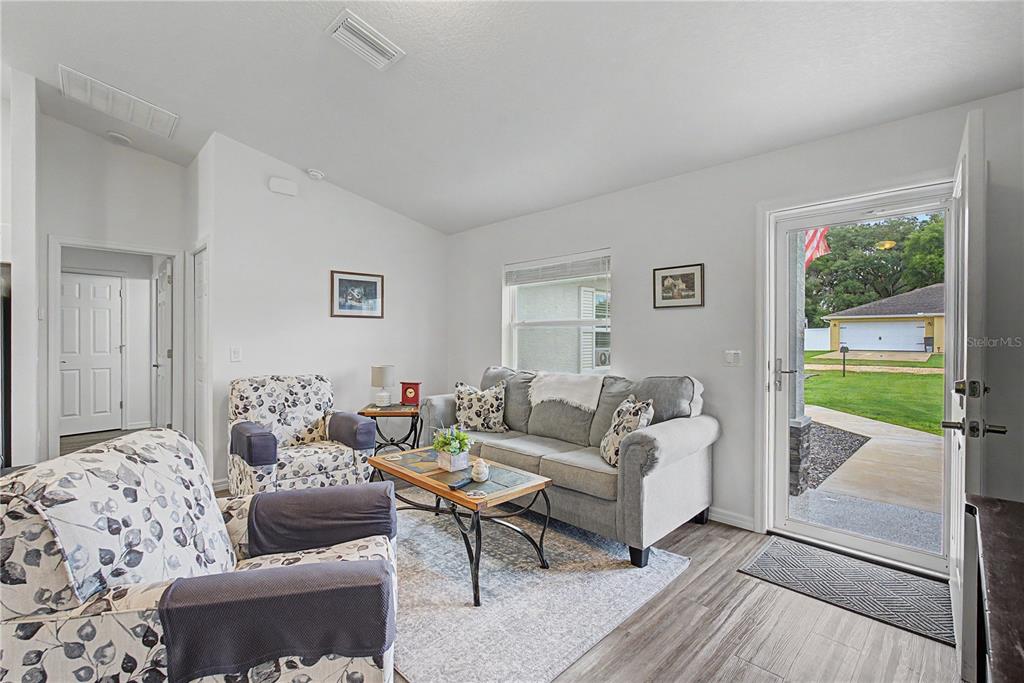 A living room features a grey sofa, patterned armchairs, a coffee table, and an open door — 4322 E MARYLAND STREET, INVERNESS, FL