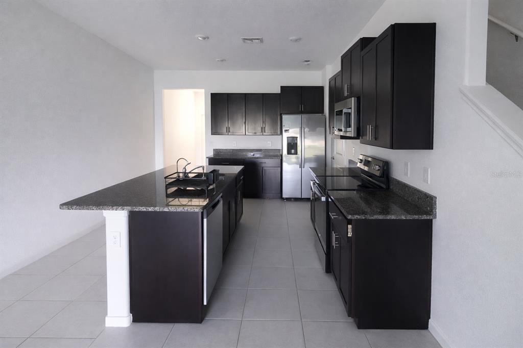 A kitchen features dark wood cabinets, granite countertops, stainless steel appliances, and a central island — 12420 CRYSTAL JADE WAY, PARRISH, FL