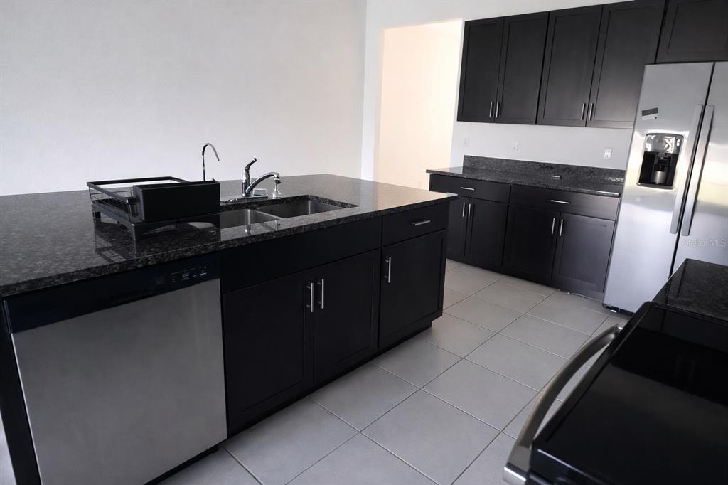 A kitchen features a dark granite island with a sink, dark cabinetry, and stainless appliances — 12420 CRYSTAL JADE WAY, PARRISH, FL