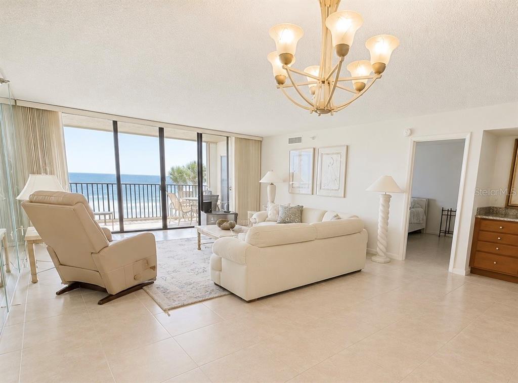 A living room with a white sofa, recliner, chandelier, and a balcony overlooking the ocean — 2675 GULF OF MEXICO DRIVE UNIT 203, LONGBOAT KEY, FL