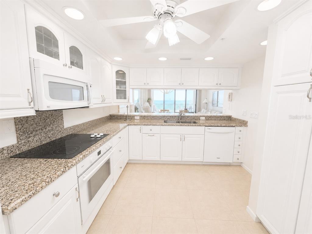 A bright kitchen features white cabinets, granite countertops, and a view of the ocean — 2675 GULF OF MEXICO DRIVE UNIT 203, LONGBOAT KEY, FL