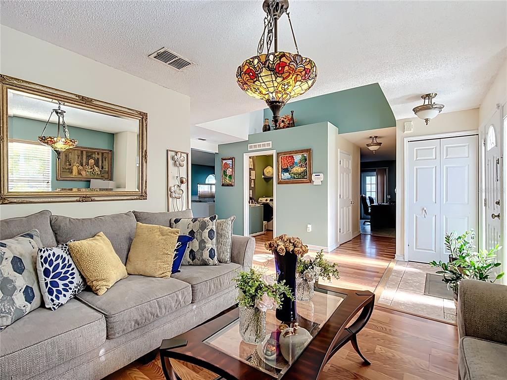 A living room features a grey sofa, a glass coffee table, and a stained-glass chandelier — 5009 STRADA DRIVE, WINTER HAVEN, FL