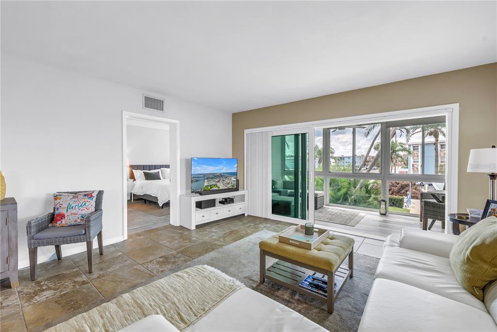 A living room with tile floors, a white sofa, and a sliding glass door to a balcony — 6201 2ND STREET E UNIT 82, ST PETE BEACH, FL