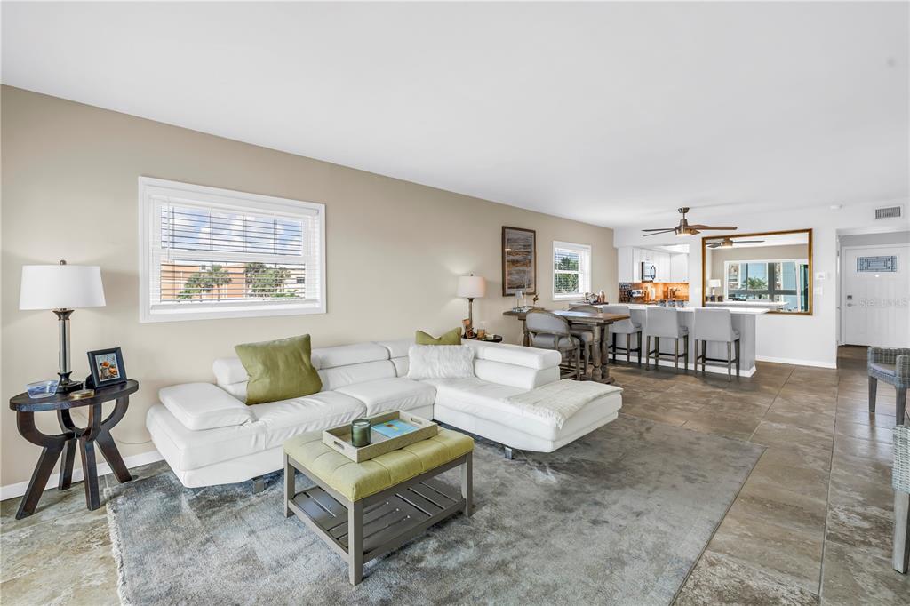 A living room with a white sectional sofa, a green ottoman, and an open kitchen — 6201 2ND STREET E UNIT 82, ST PETE BEACH, FL