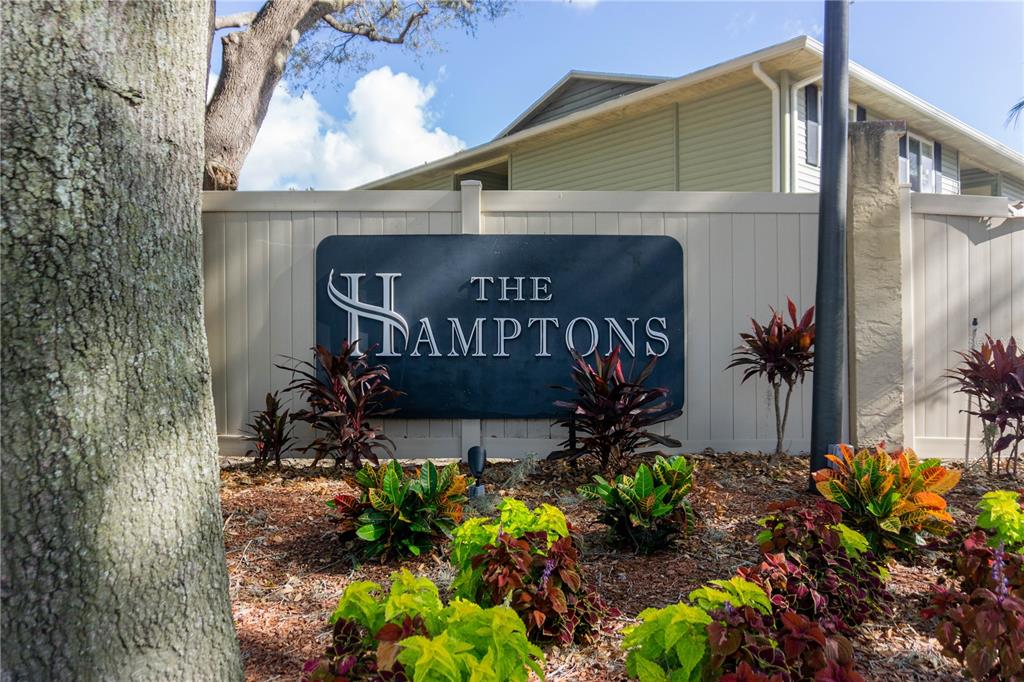 A sign for The Hamptons stands in front of a tan fence and landscaping — 231 BERRY TREE PLACE, BRANDON, FL