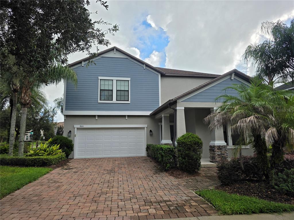 A two-story house features a blue-sided upper level, a brick driveway, and a two-car garage — 8001 POND APPLE DRIVE, WINTER GARDEN, FL