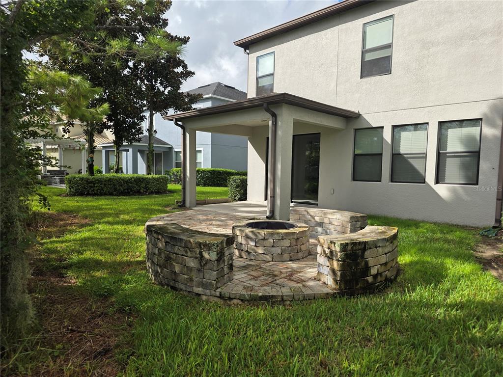 A backyard patio features a stone fire pit with curved seating walls and a covered porch — 8001 POND APPLE DRIVE, WINTER GARDEN, FL