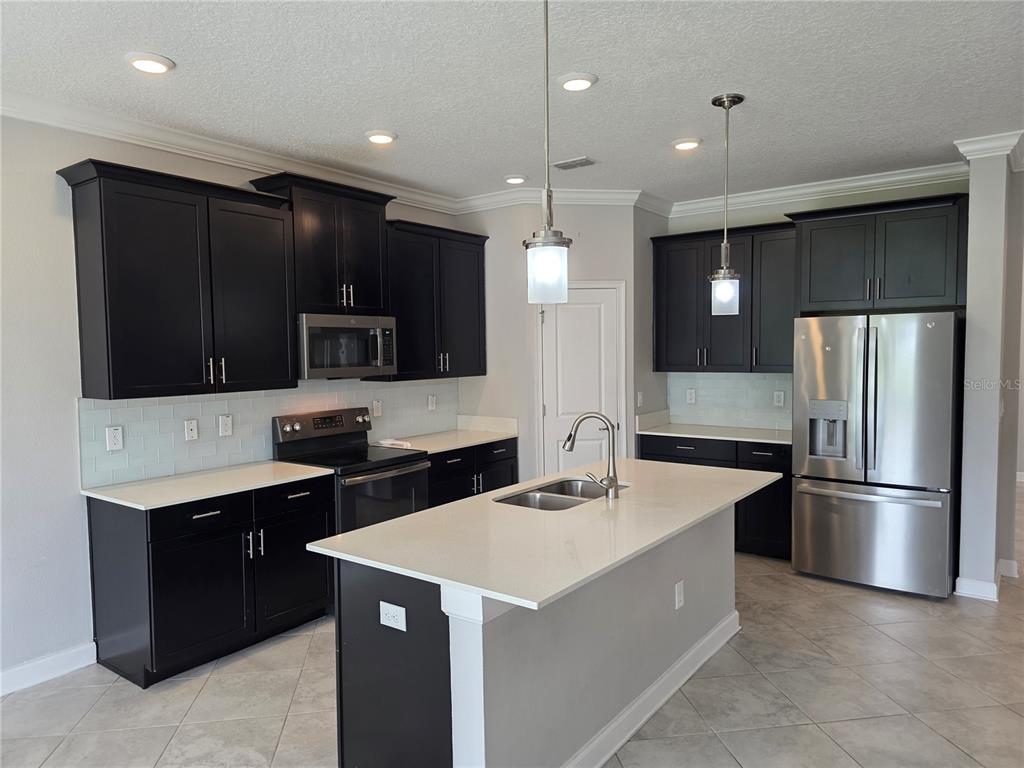 A kitchen features dark cabinets, stainless steel appliances, a central island, and light-colored countertops — 8001 POND APPLE DRIVE, WINTER GARDEN, FL