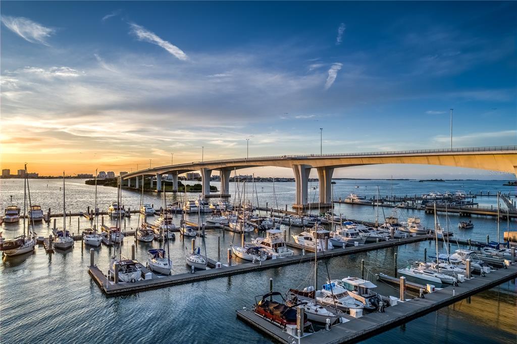 A marina filled with sailboats and motorboats sits beneath a large concrete bridge at sunset — 331 CLEVELAND STREET UNIT 213, CLEARWATER, FL
