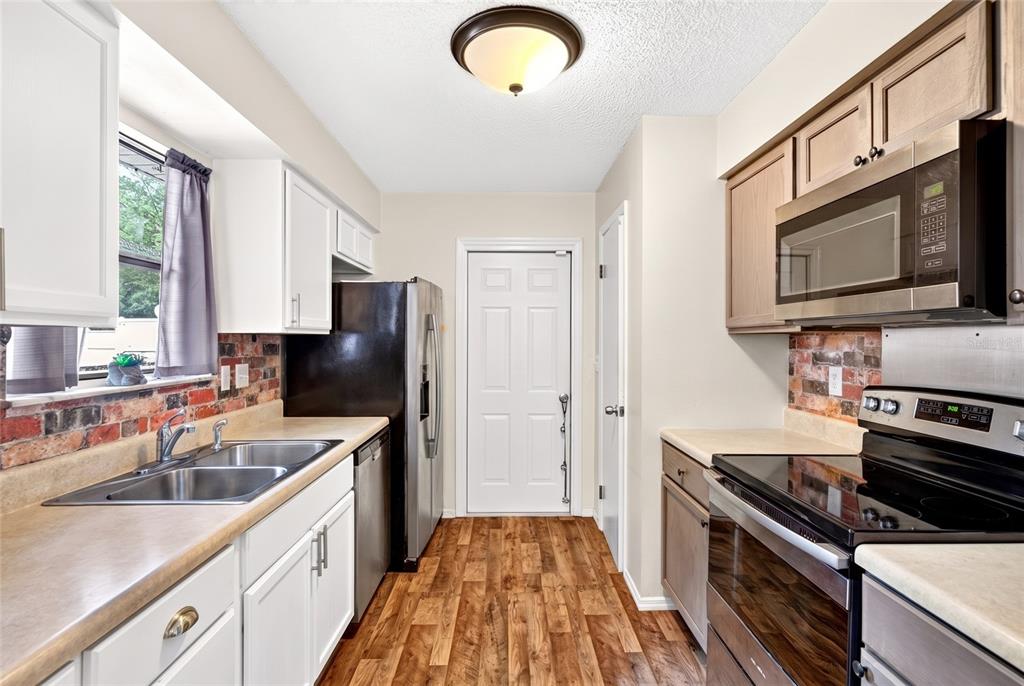 A kitchen features white and wood cabinets, stainless steel appliances, and a brick backsplash — 27 CEDAR TRACE, OCALA, FL