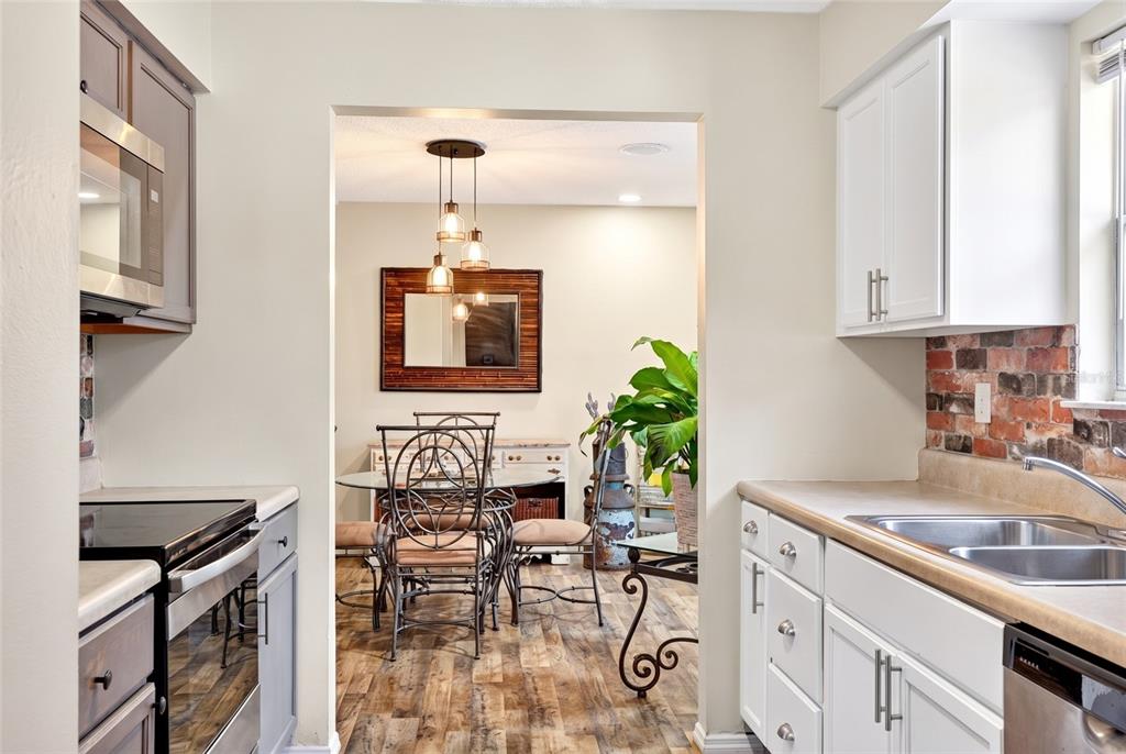 A kitchen with gray and white cabinets leads into a dining room with wood flooring — 27 CEDAR TRACE, OCALA, FL