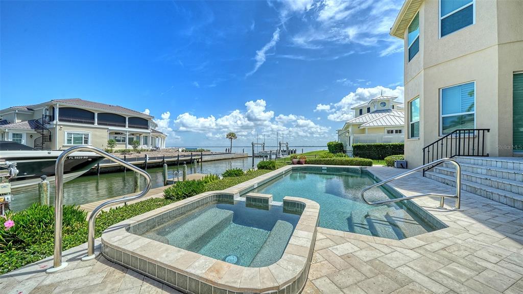 A backyard swimming pool and hot tub overlook a canal with a boat and houses — 657 HALYARD LANE, LONGBOAT KEY, FL