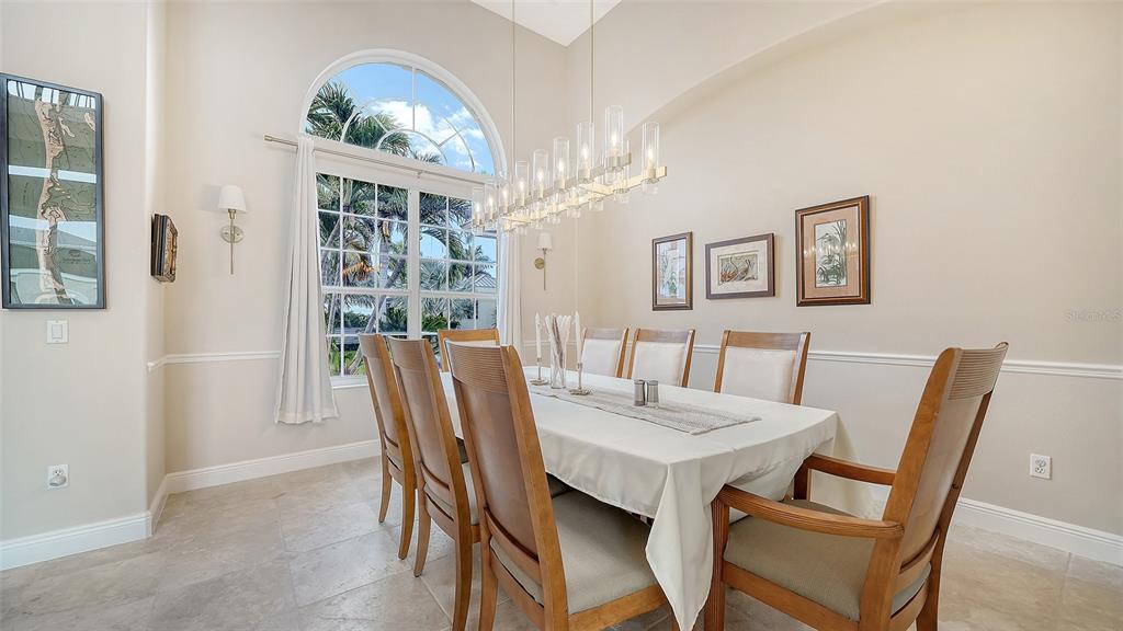 A dining room features a long table, wooden chairs, a chandelier, and a large arched window — 657 HALYARD LANE, LONGBOAT KEY, FL