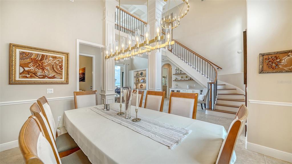 A dining room features a long table, a modern chandelier, and a staircase with railings — 657 HALYARD LANE, LONGBOAT KEY, FL