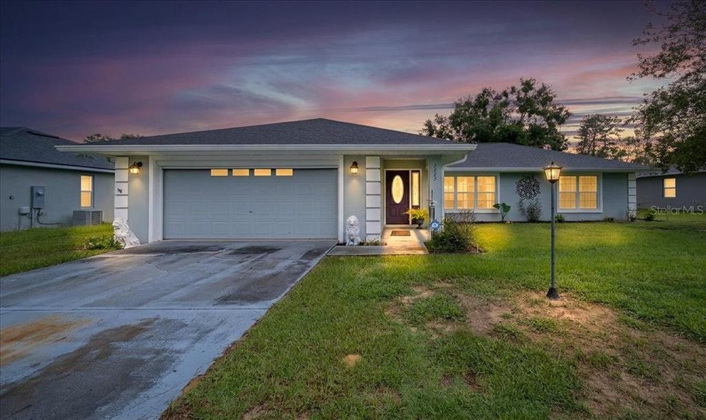 A single-story house with a two-car garage, light blue siding, and a paved driveway at dusk — 2222 SW 167TH PLACE, OCALA, FL