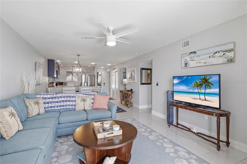 A living room features a ceiling fan, a television, and sliding doors overlooking the water — 1801 GULF DRIVE N UNIT 142, BRADENTON BEACH, FL