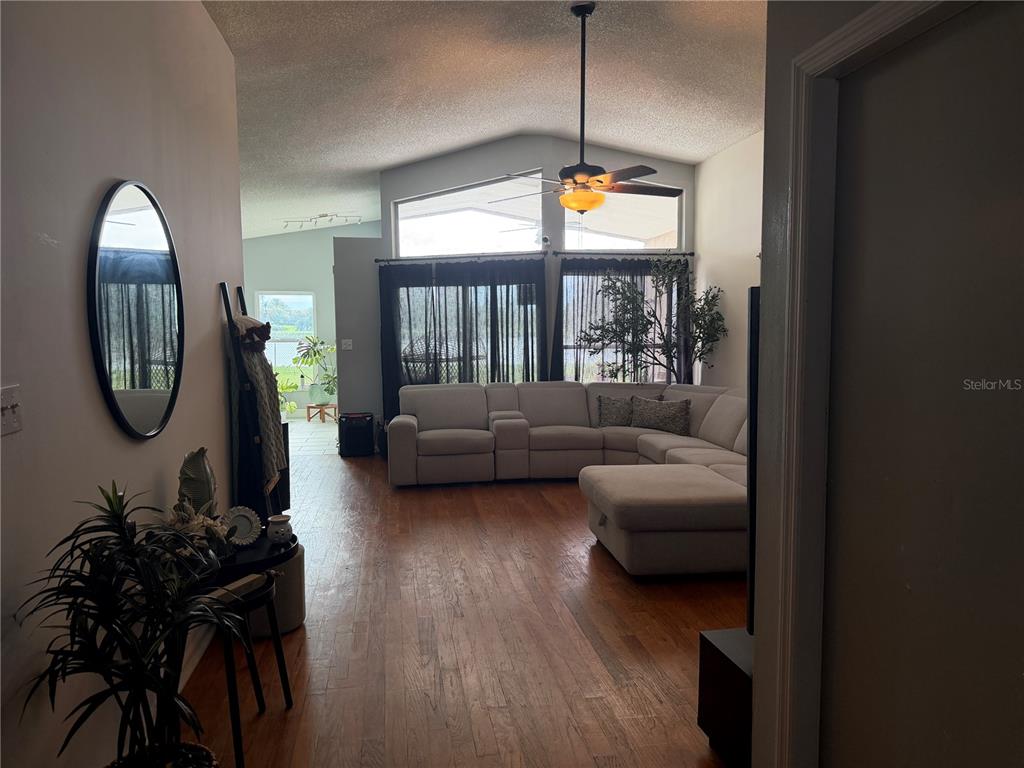 A living room with hardwood floors, a sectional sofa, and large windows overlooking a lake — 3236 KOVAL COURT, ORLANDO, FL
