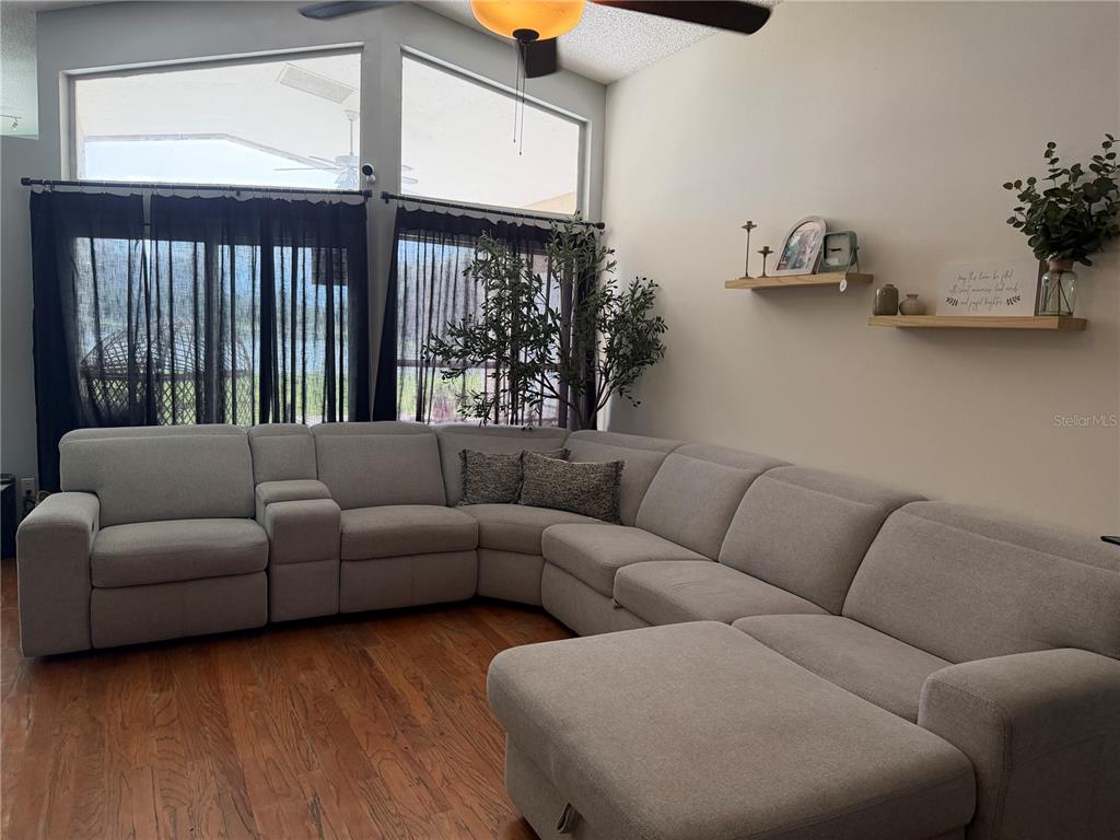 A living room features a large light gray sectional sofa, wood flooring, and two wall shelves — 3236 KOVAL COURT, ORLANDO, FL