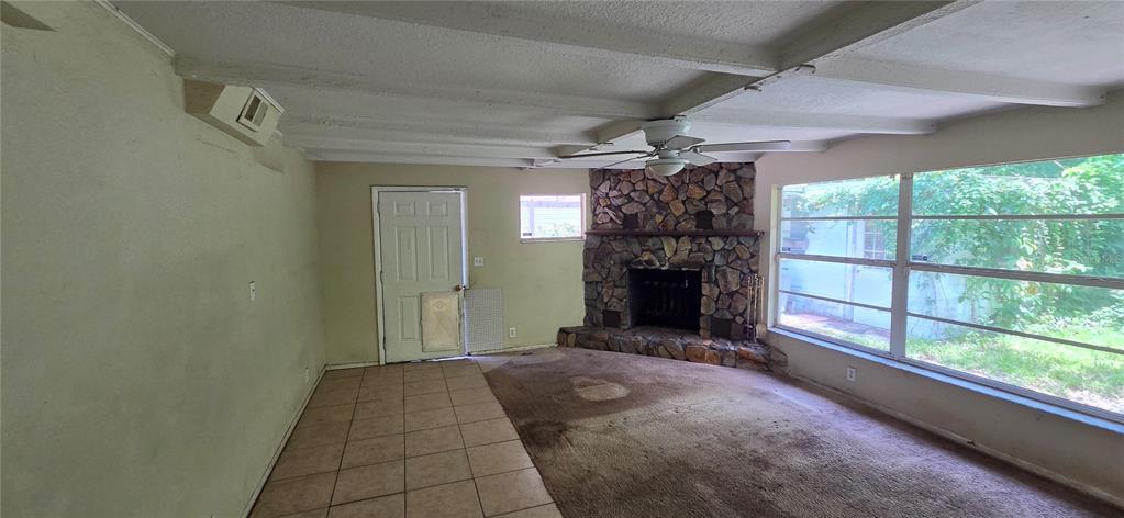 A living room features a stone fireplace, carpeted flooring, a tiled entryway, and exposed beams — 8944 MARIGOLD DRIVE, NEW PORT RICHEY, FL