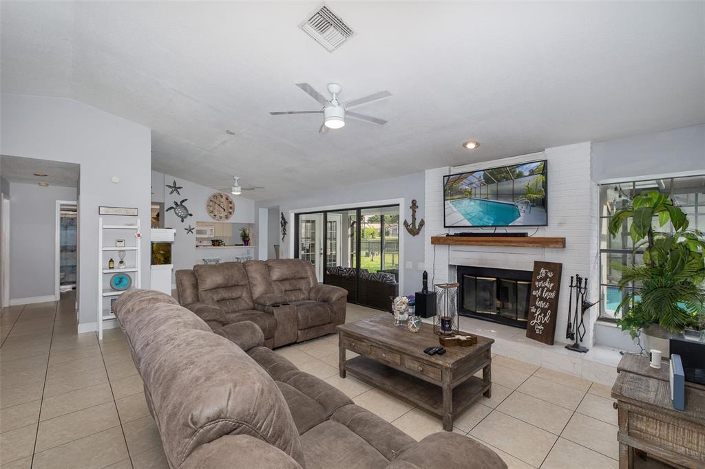 A living room with tile floors, a brick fireplace, and a view of a pool — 13316 BRIGHAM LANE, HUDSON, FL