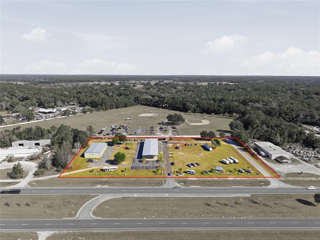 An aerial view shows two commercial buildings on a large, flat, grassy lot — 20761 NE HIGHWAY 27, WILLISTON, FL