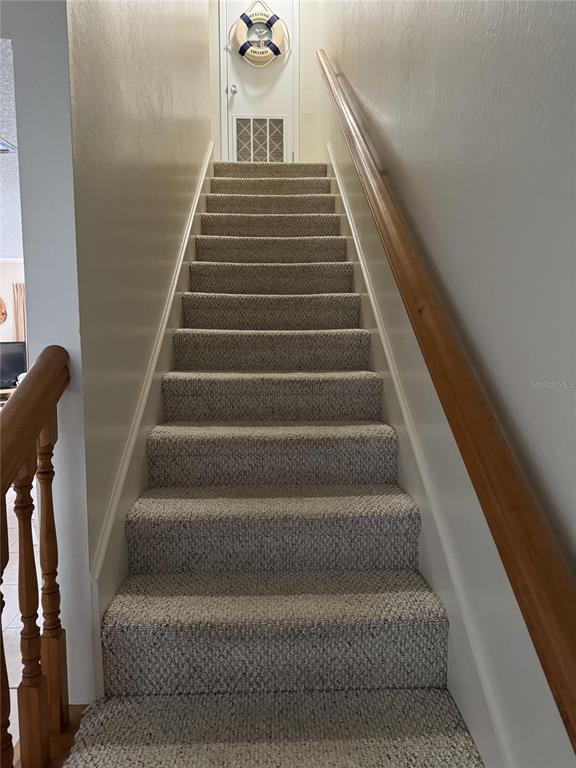 A straight staircase with carpeted steps and a wooden handrail leads to a landing — 815 OCEAN SHORE BOULEVARD UNIT 10B, ORMOND BEACH, FL