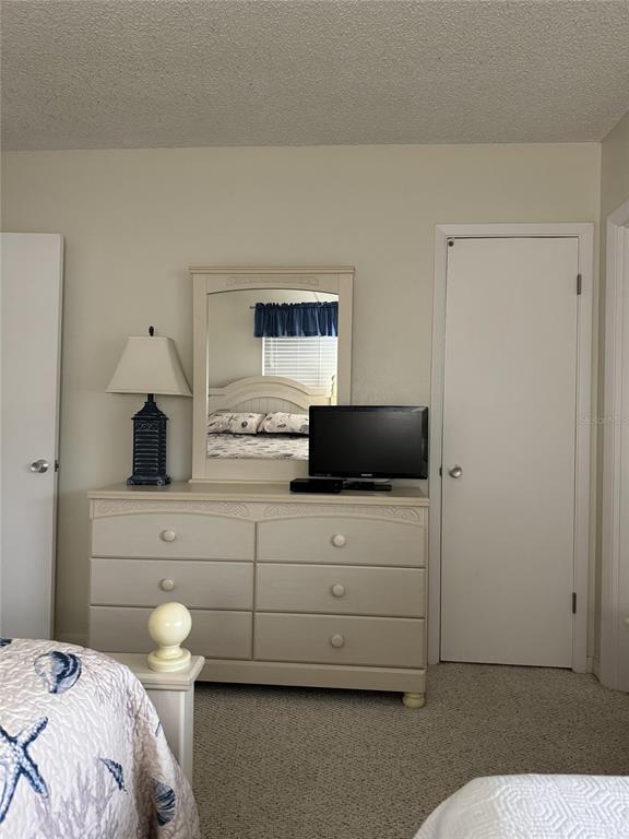A bedroom features a light-colored dresser with a mirror, a lamp, and a television — 815 OCEAN SHORE BOULEVARD UNIT 10B, ORMOND BEACH, FL