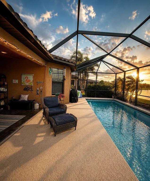 A screened-in patio features a swimming pool, wicker furniture, and a view of the sunset — 10319 SAINT FRANCIS TERRACE, PALMETTO, FL