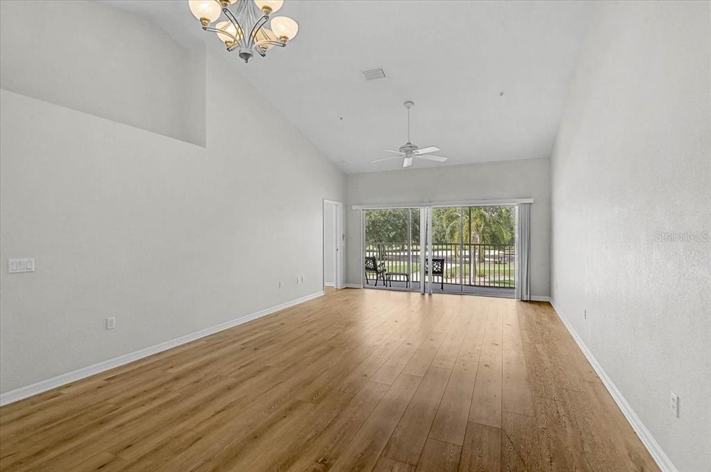 An empty living room with vaulted ceilings, light wood flooring, and a sliding glass door — 6870 FAIRVIEW TERRACE, BRADENTON, FL