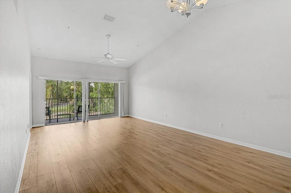 An empty living room features light wood-look flooring, white walls, a vaulted ceiling, and sliding doors — 6870 FAIRVIEW TERRACE, BRADENTON, FL